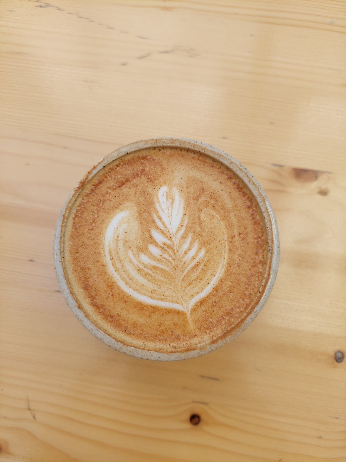 Flat white et son latte art, servi dans une tasse en grès sur une table en pin clair