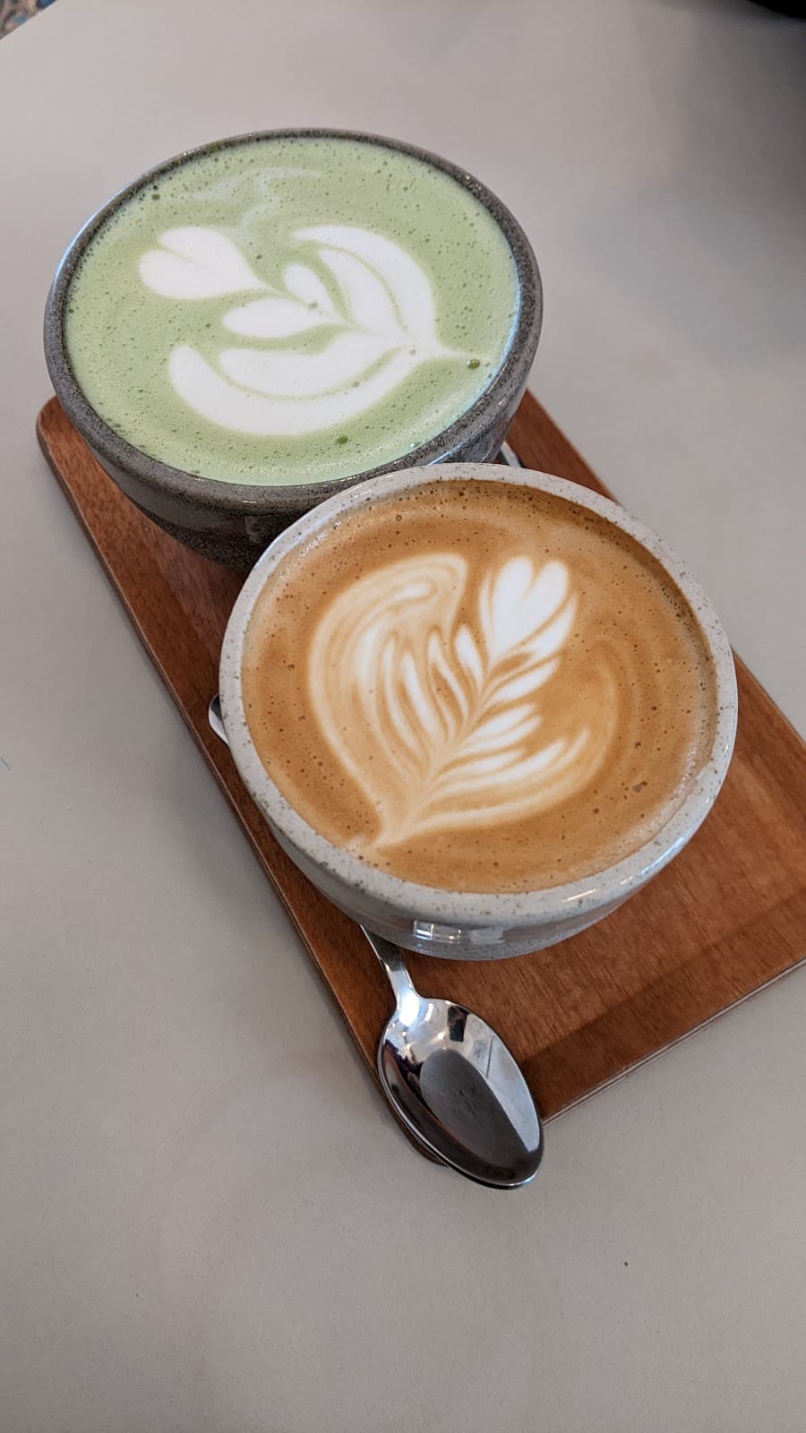 Matcha latte et flat white côte à côte sur une planche en bois, tasses en céramique mouchetée