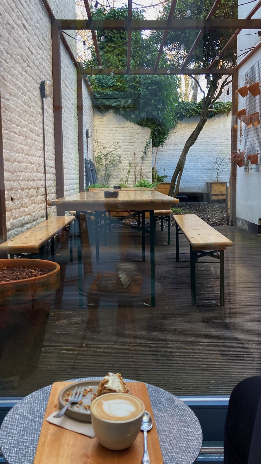 Depuis la salle, la baie vitrée s'ouvre sur le jardin : tables en bois, murs blanchis et lierre